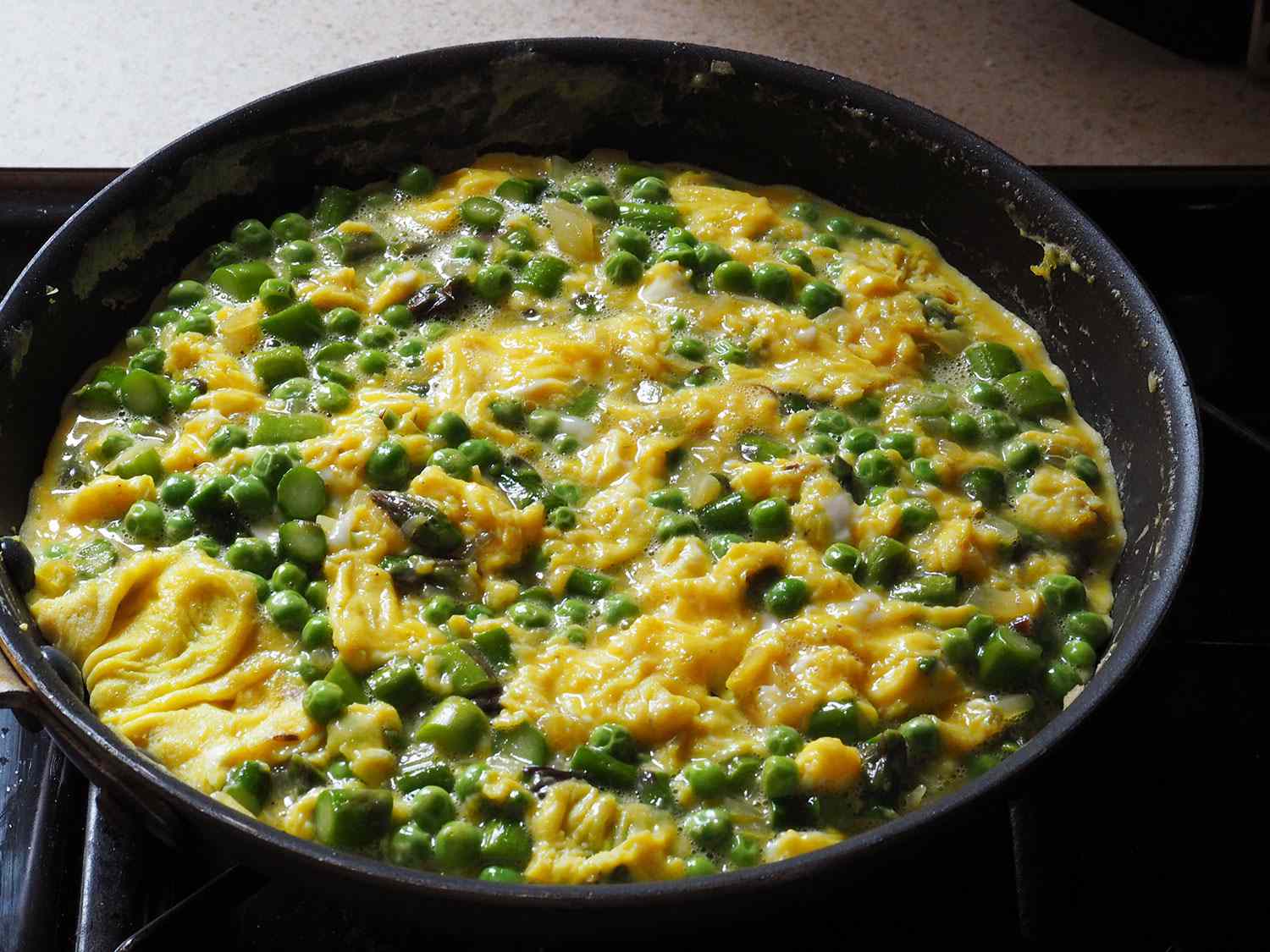 The eggs have been thoroughly combined with the sautéed vegetables. The egg has thickened but is still moist-looking on the surface.