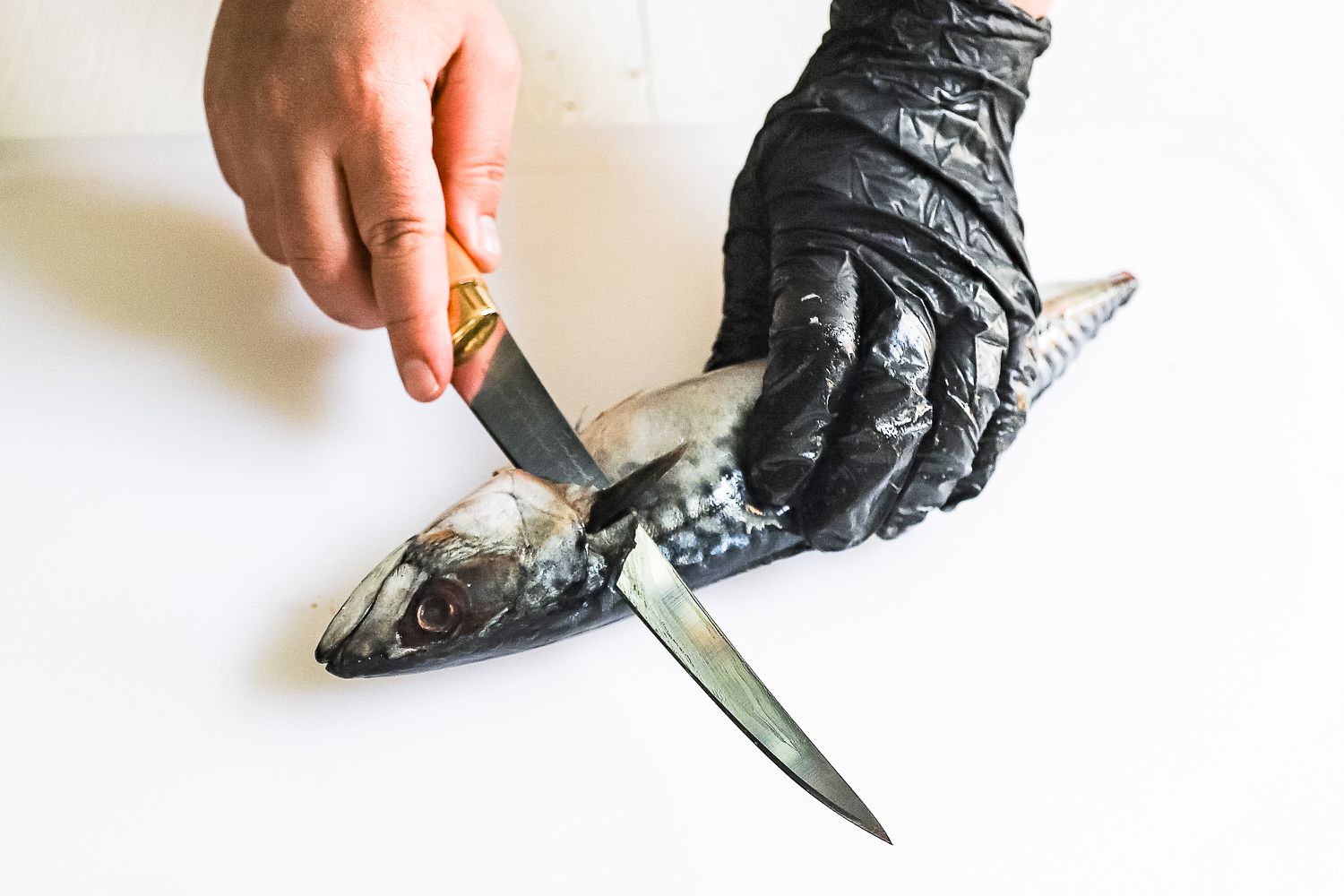 A person preparing a fish with knives on a cutting board