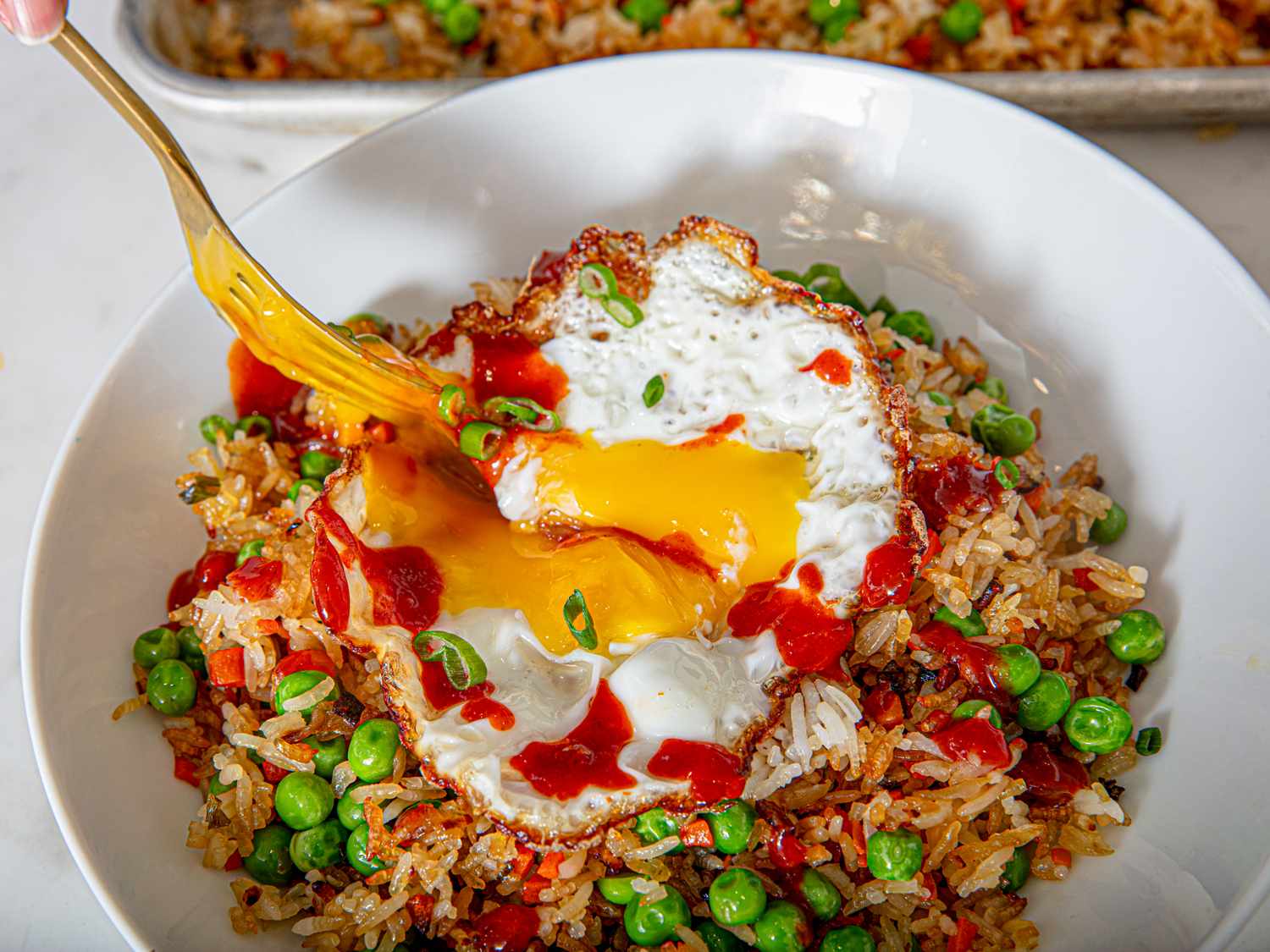Fried rice garnished with peas, topped with a fried egg being broken with a fork