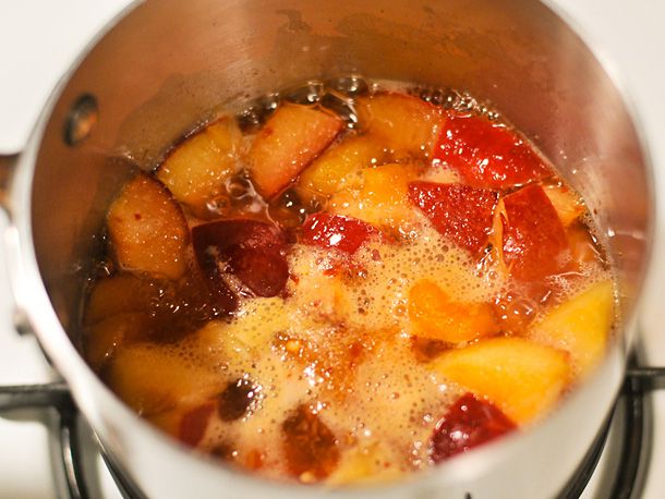 All of the ingredients for duck sauce simmering in a saucepan. The liquid is bubbling and the apricot pieces are floating.