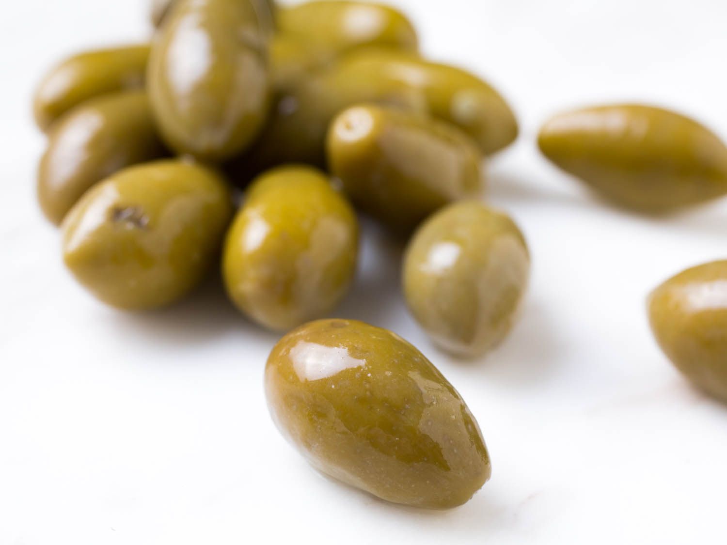 Closeup of shiny, green almond-shaped olives on white surface