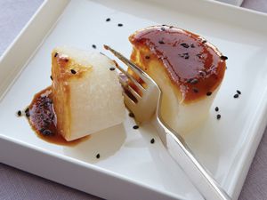 Braised daikon radish on a square plate, sprinkled with black sesame seeds.