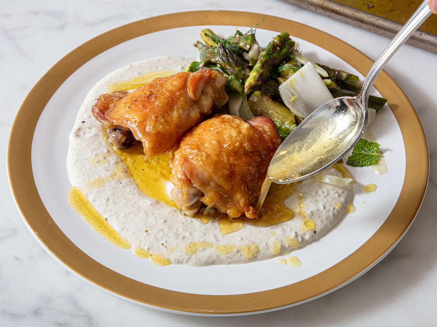 A plated dish with chicken thighs, sauce, and asparagus on a white and gold plate