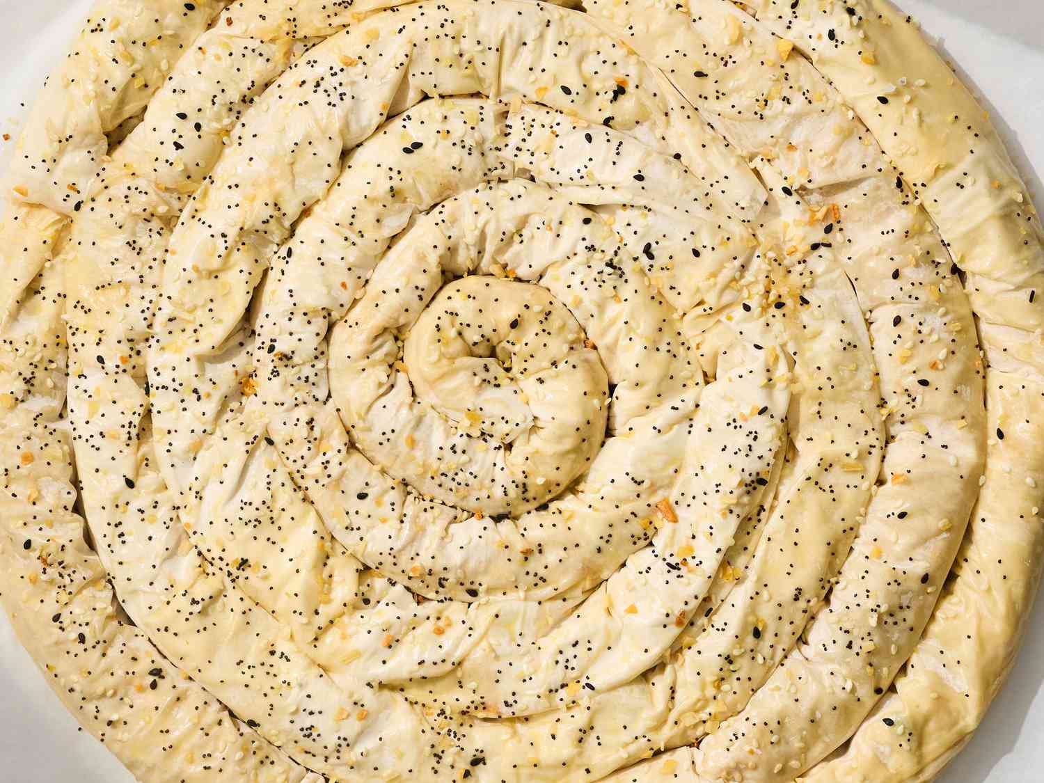 A spiraled pastry dough sprinkled with seeds and prepared for baking, presented in a dish