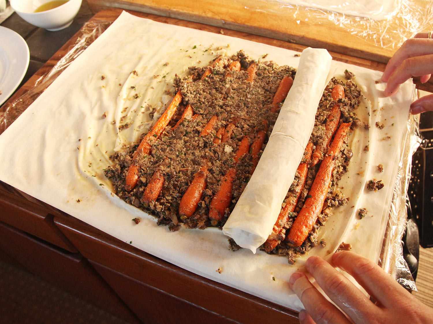 Rolling bean-filled phyllo log into phyllo sheet with carrots and duxelles.