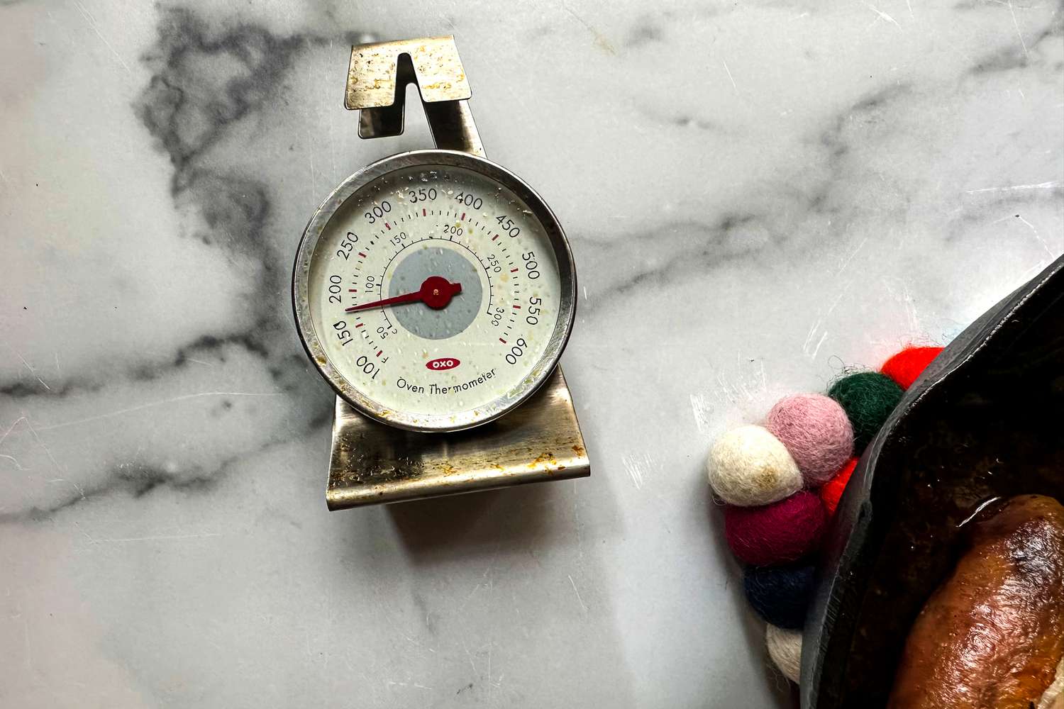 The OXO Oven thermometer on a marble surface next to a cast iron pan.