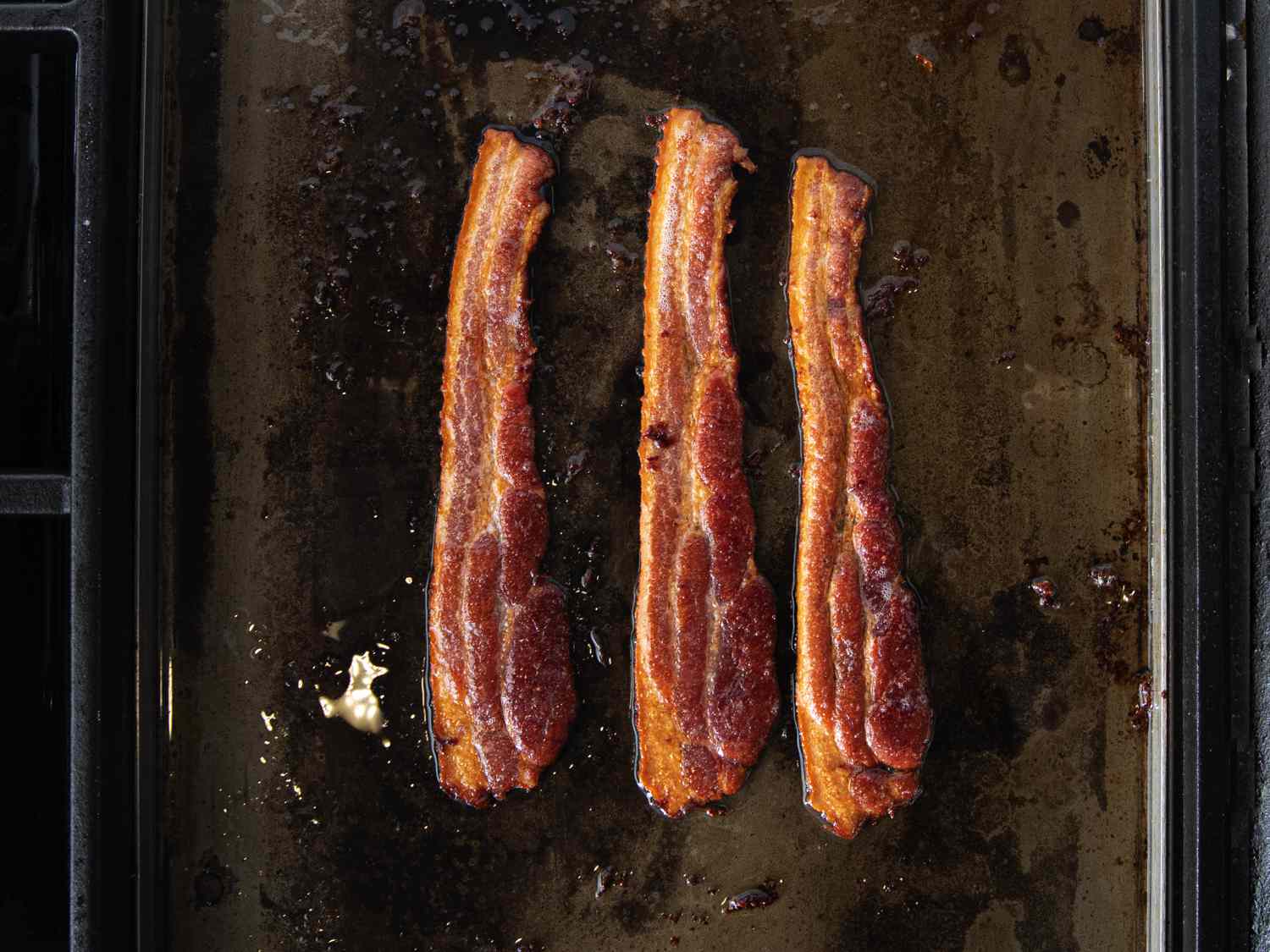 3 pieces of bacon sizzling on a griddle