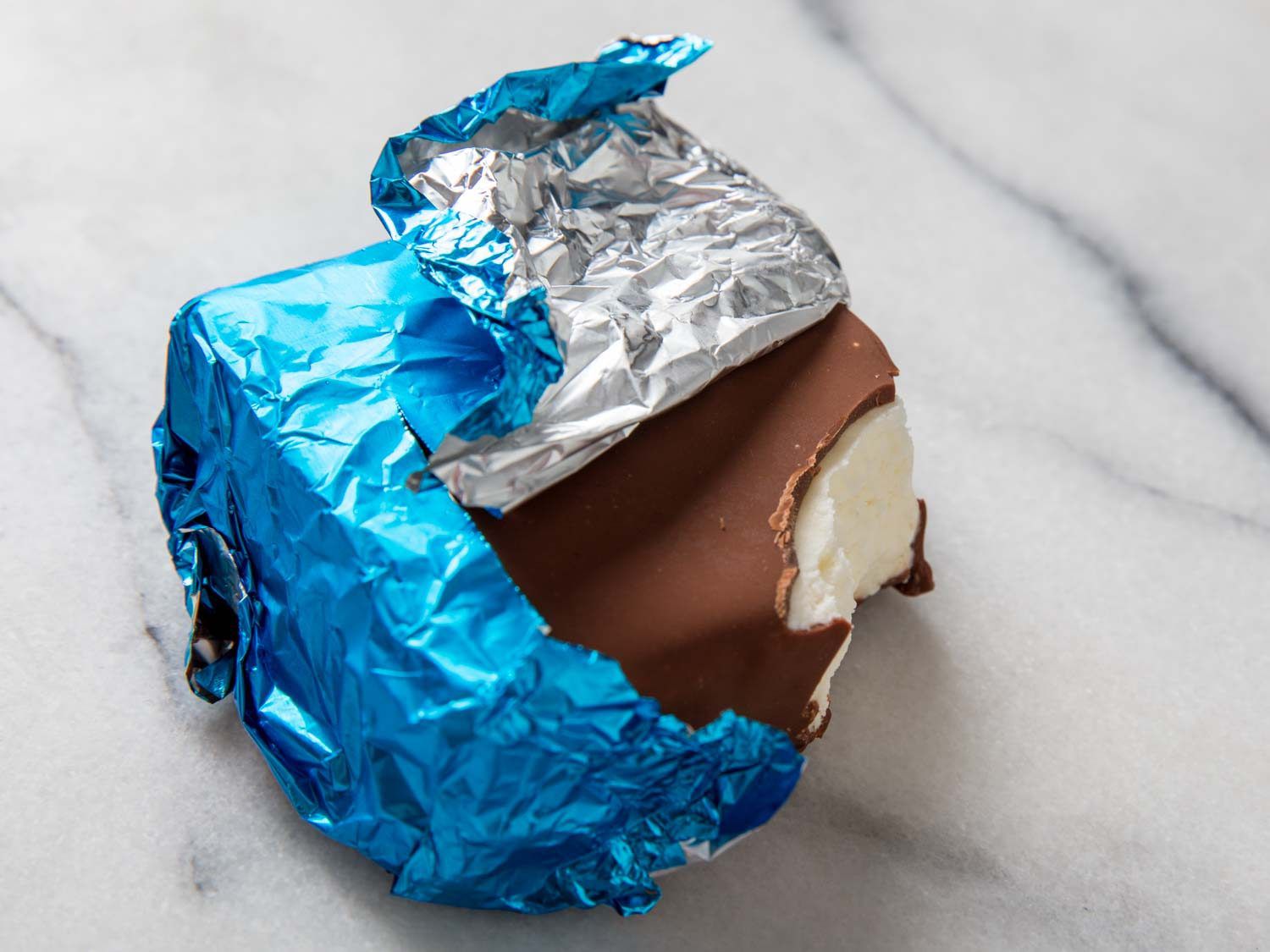 A homemade Klondike Bar wrapped in blue foil with a bite out of it.