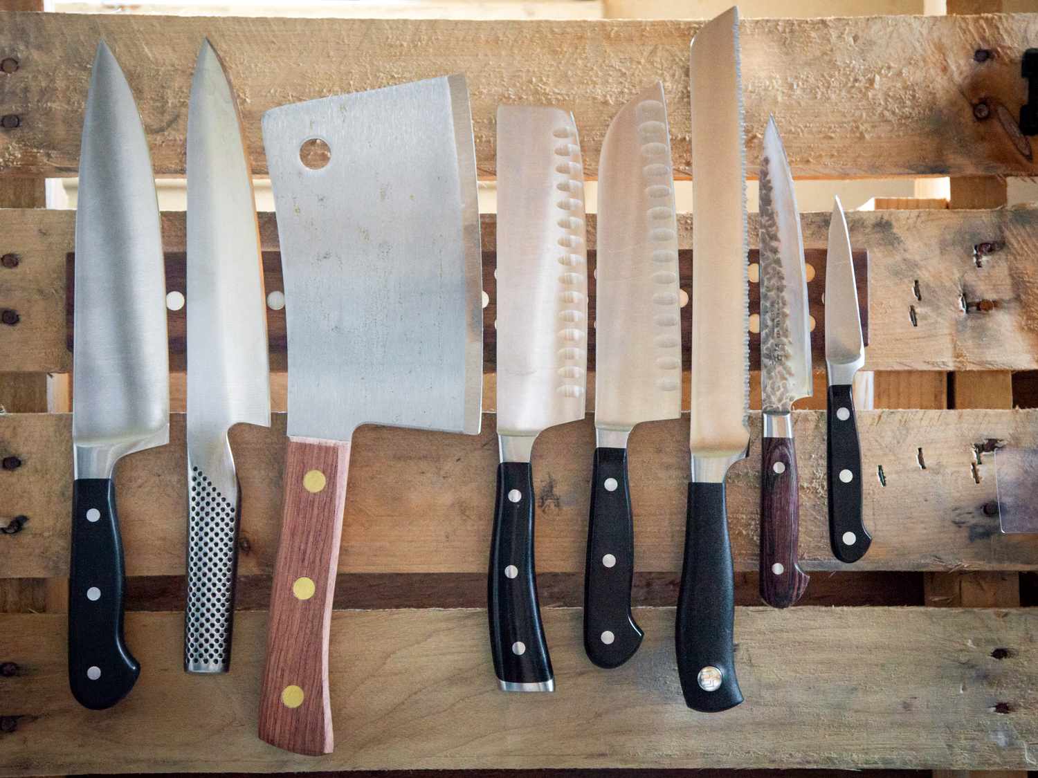 A magnetic knife bar with several knives on it affixed to a wooden pallet