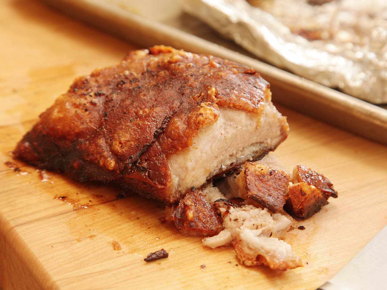 A closeup of a chunk of the finished pork belly, crisped and ready to slice on a wooden cutting board.