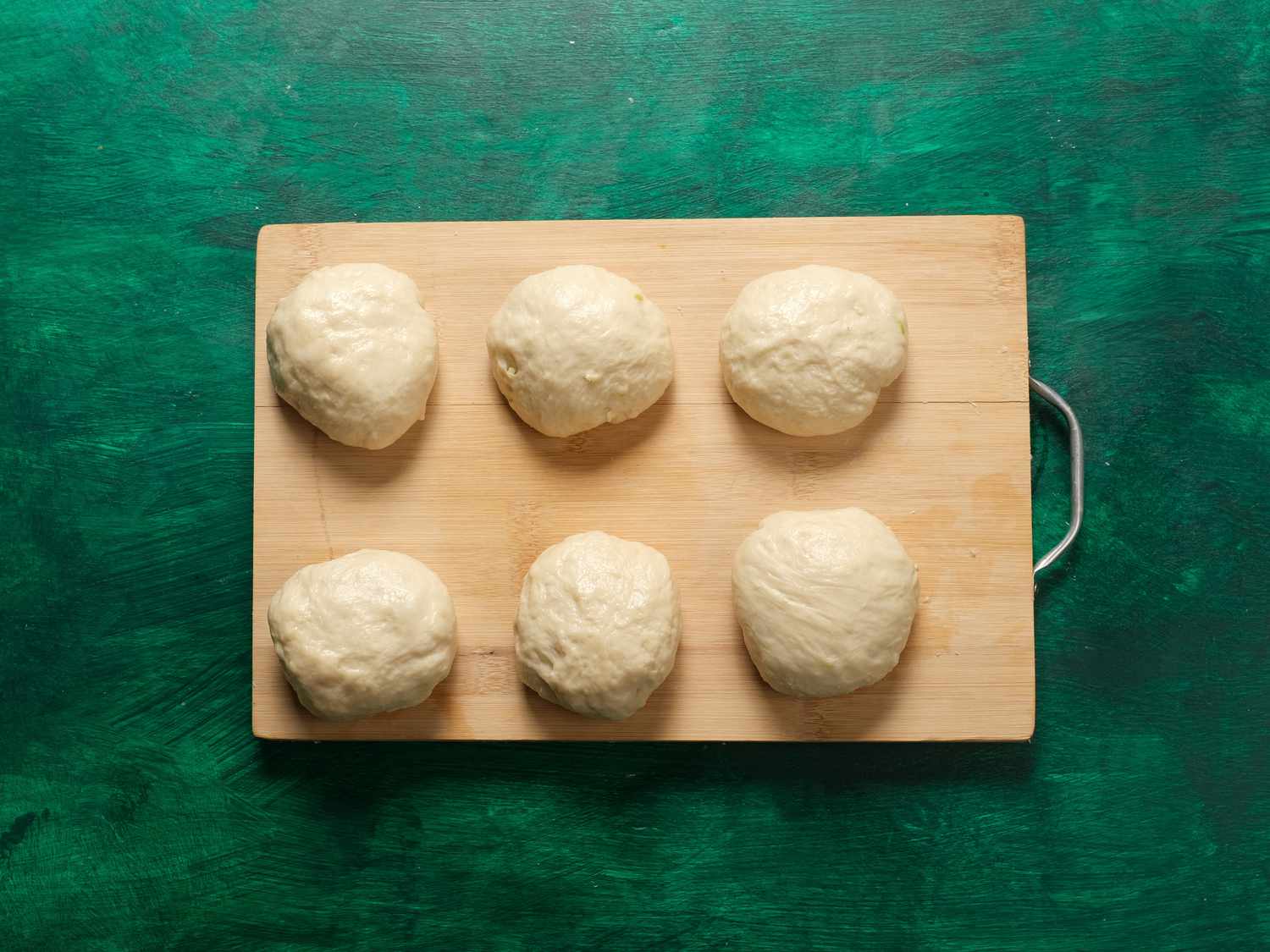 Dough divided into 6 balls on a wooden board and green surface 
