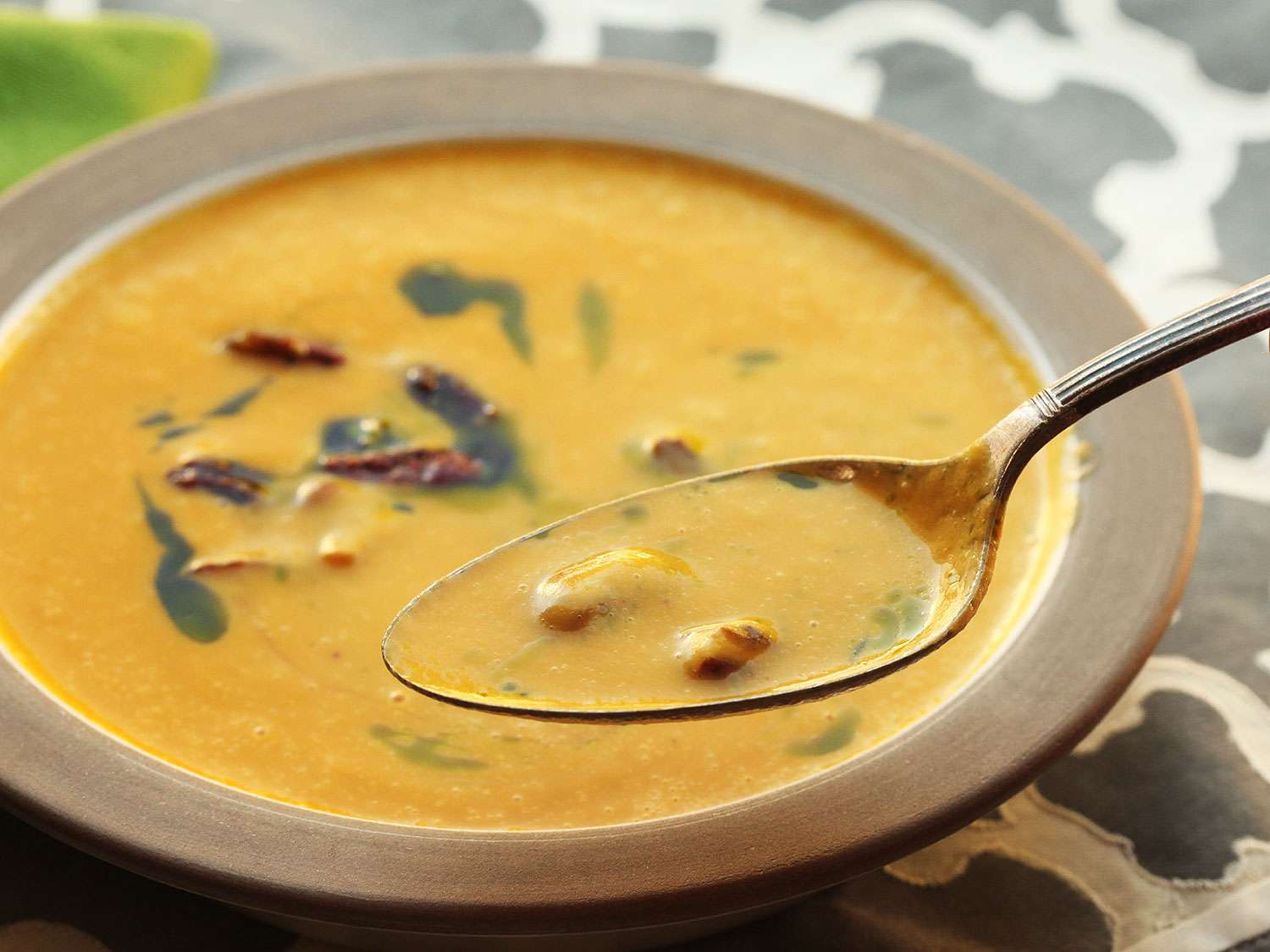 Lifting a spoon of butternut squash soup that's been drizzled with sage oil and garnished with candied pecans.