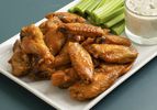 Oven-fried buffalo wings on a white rectangular plate with celery sticks and a glass cup of bleu cheese dressing.