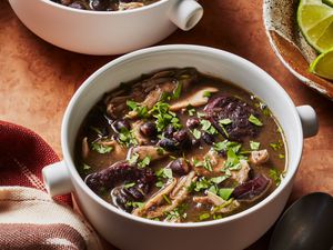 2 mugs of chicken and black bean soup with a bowl of limes on the side. 