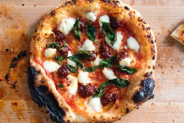 Charred pizza with 'nduja on wooden surface