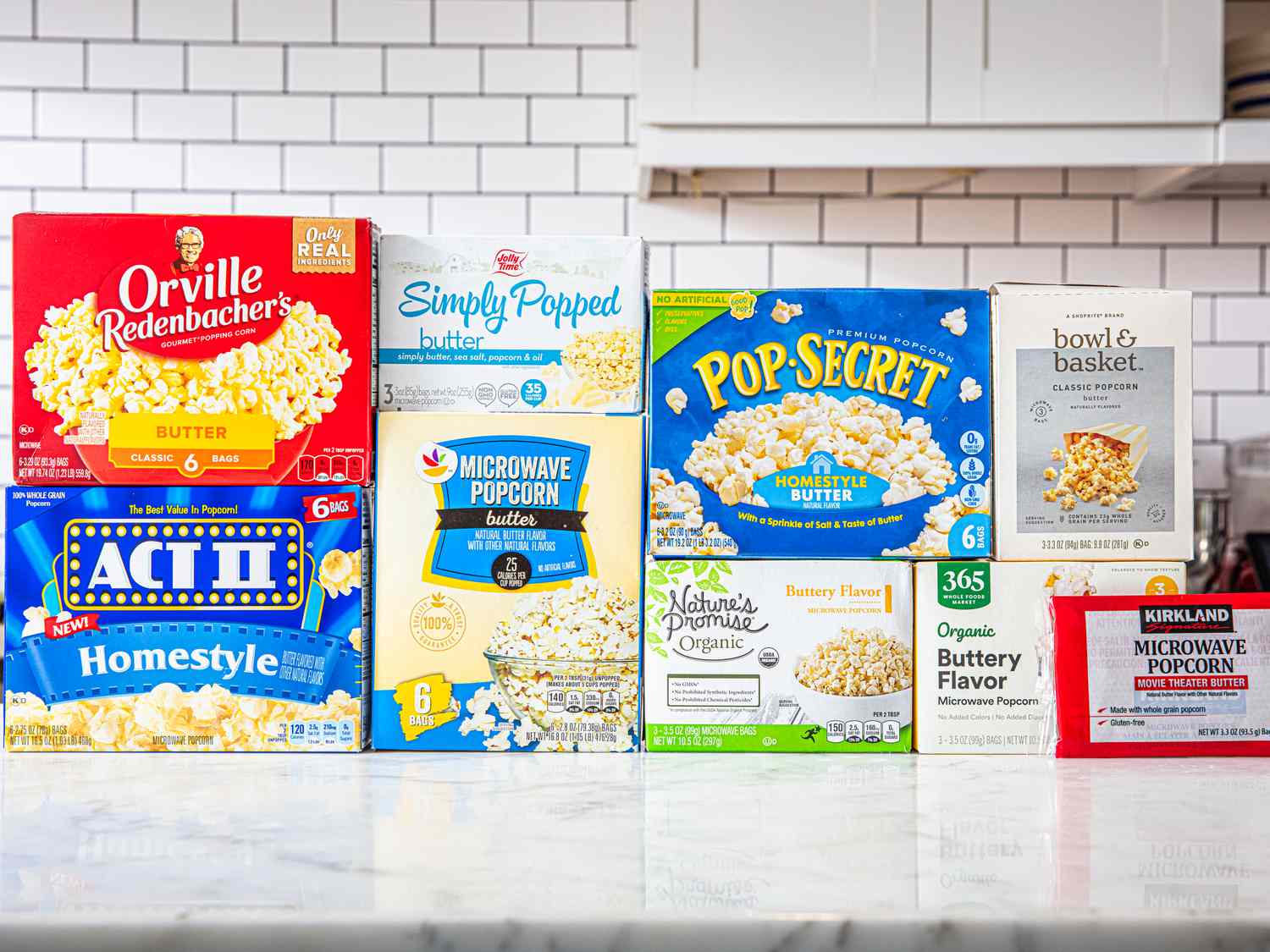 Several microwave popcorn packages displayed side by side on a kitchen countertop, including brands like Orville Redenbacher, Pop Secret, and Kirkland