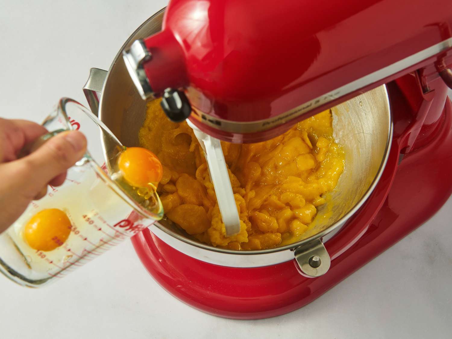 Adding eggs to choux batter in the bowl of a stand mixer.