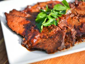 Sliced beef brisket with apricot-cranberry sauce, garnished with parsley leaves on white platter
