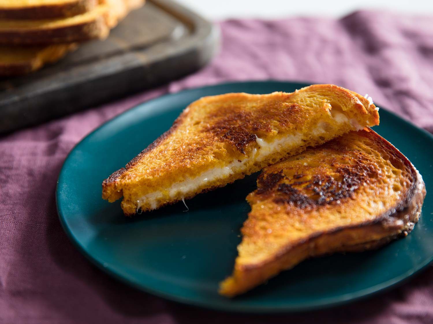 A grilled cheese sandwich made with pumpkin sandwich bread, sliced into triangles, on a blue plate on a purple tablecloth.