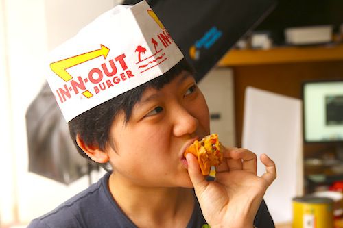 A burger taster evaluating a bite whilst wearing an In-n-Out hat.