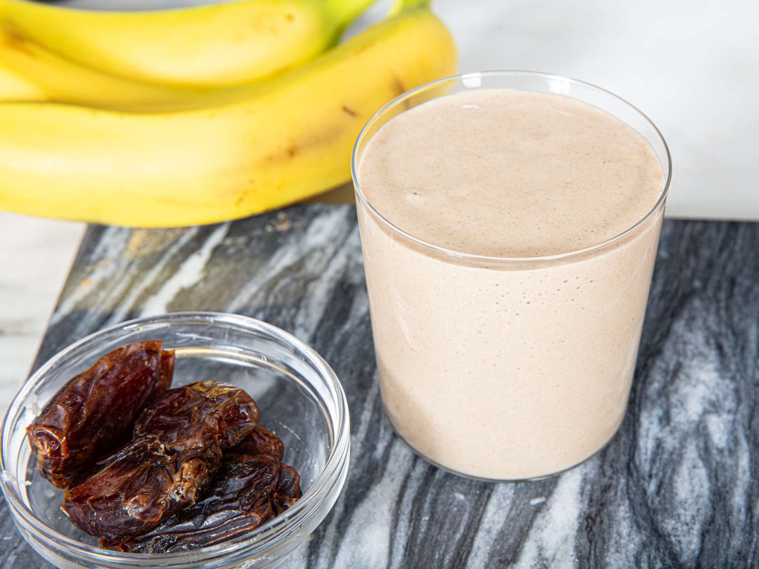 A bananadate smoothie in a glass bananas and dates beside it