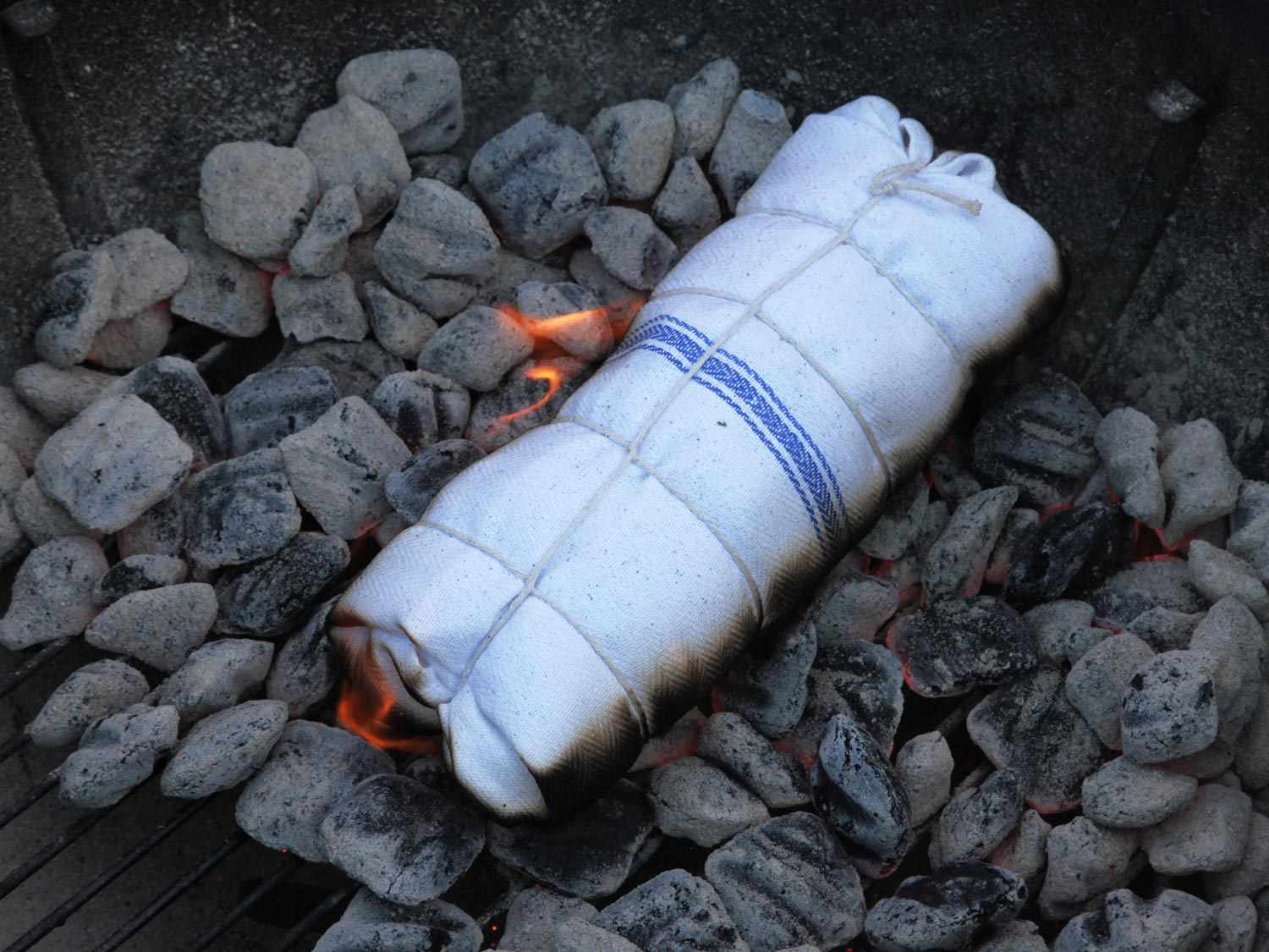 The wrapped roast has been placed on the lit coals and started to catch on fire.