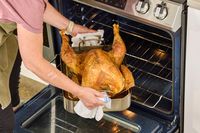 A person removing a Grassland Beef Pasture Raised Turkey from an oven