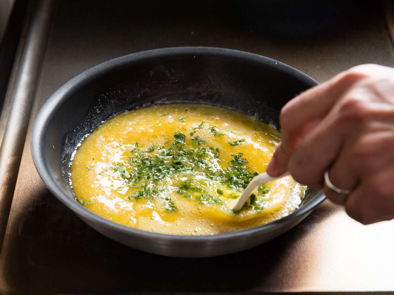 Mixing chopped herbs into eggs in a skillet.