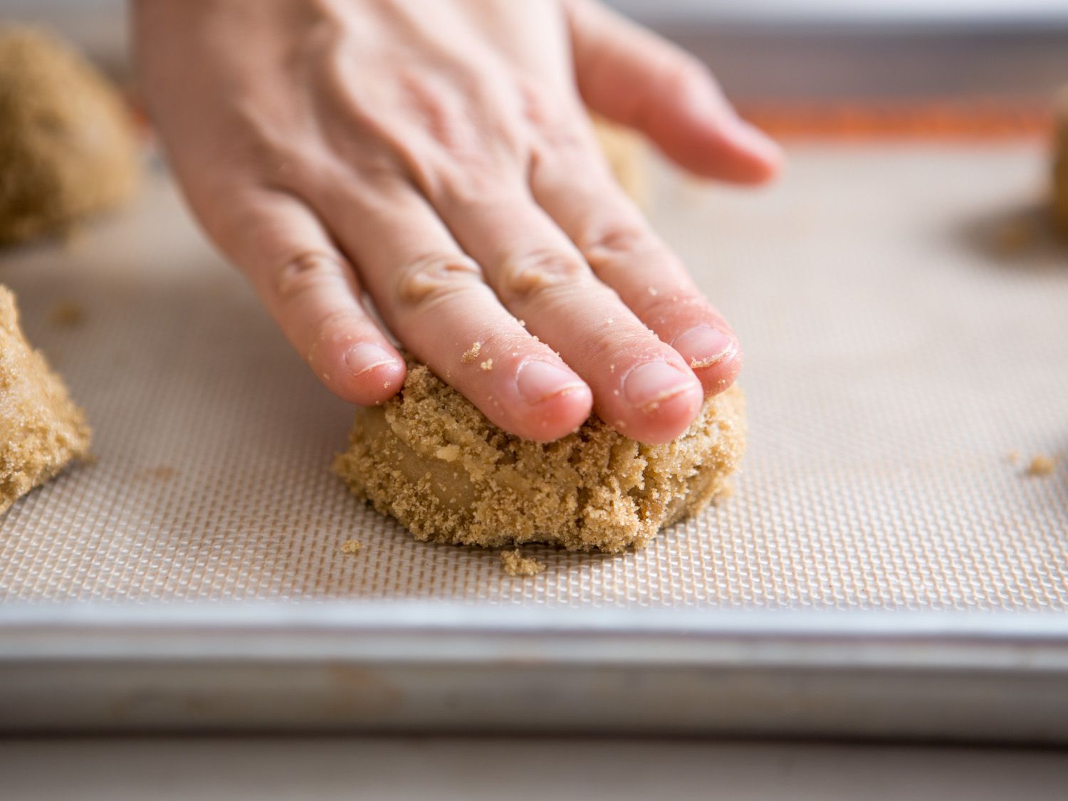 A hand pressing down on brown sugar cookie dough on a baking sheet