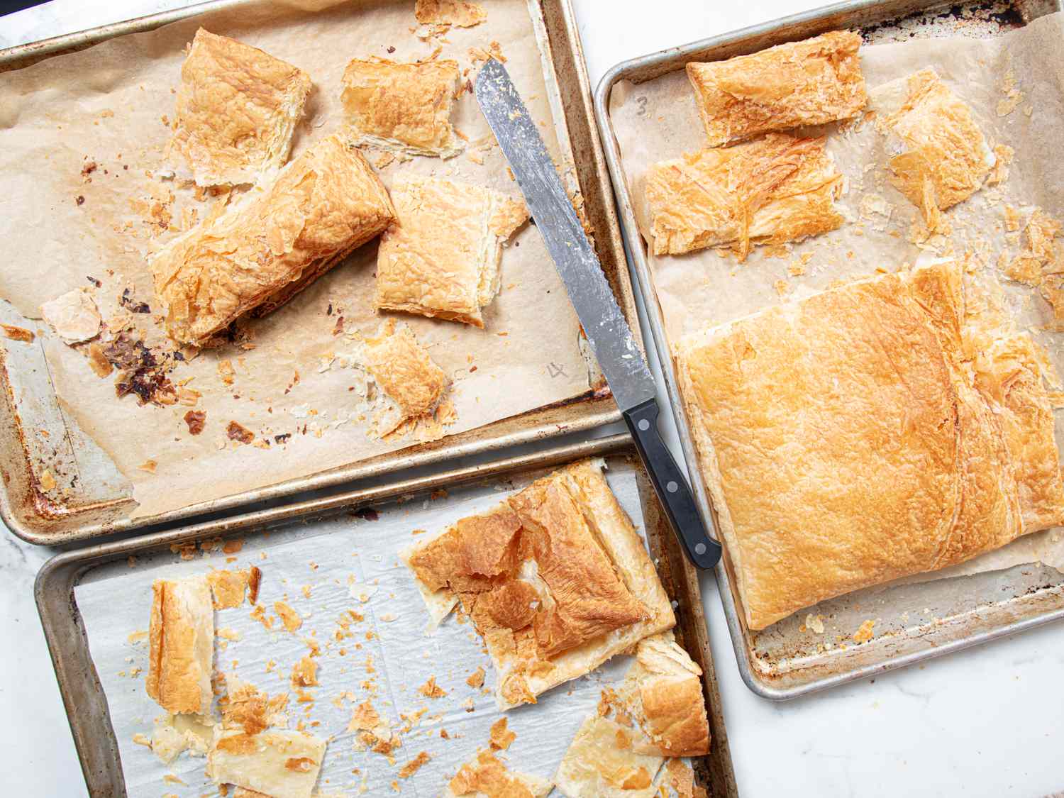 Assorted puff pastry pieces on baking trays with a knife on the side