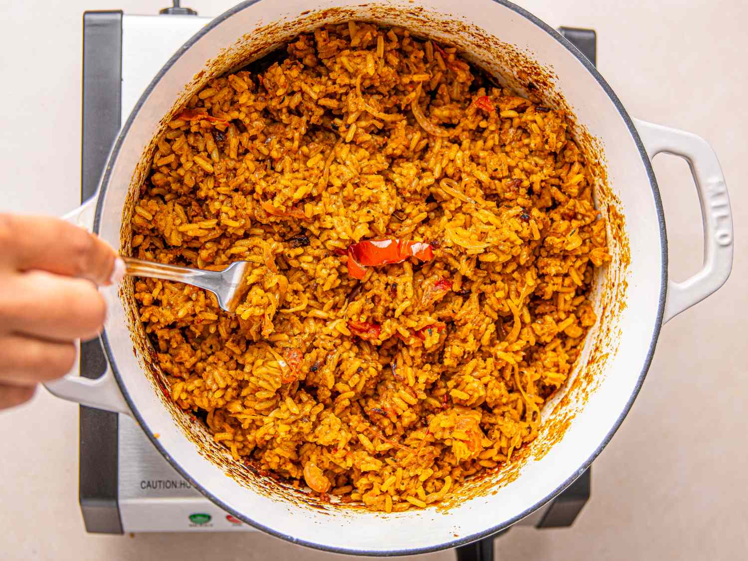 Cooked rice dish being stirred with a spoon in a pot appearing to be Nigerian jollof rice