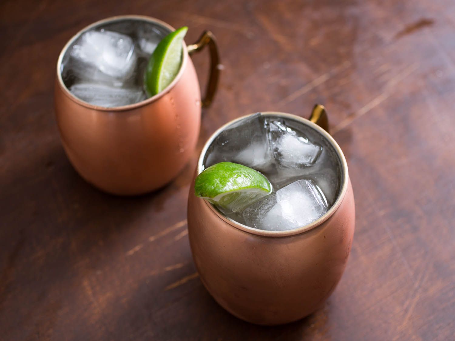 Two Moscow mule cocktails in copper mugs garnished with lime wedges.
