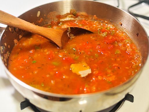 A saucepan containing Creole sauce on the stove. A pat of butter is being melted into the sauce. 