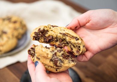 Person breaking open a gooey chocolate chip cookie in their hands