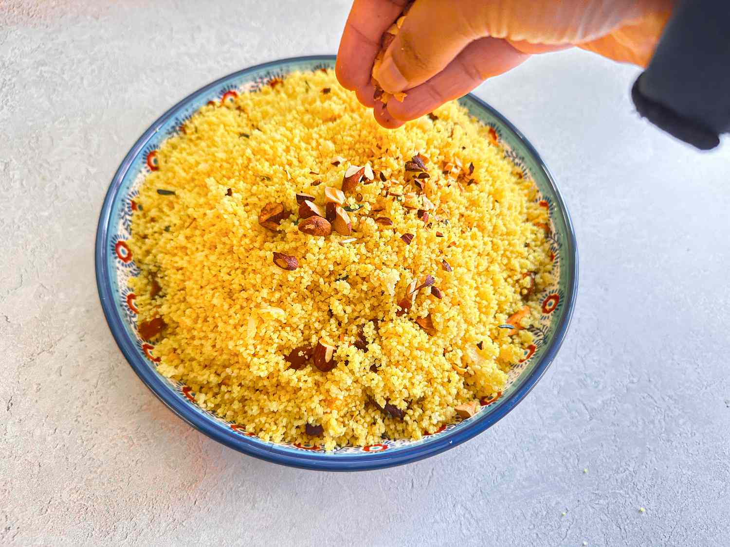 Hand sprinkling nuts over couscous in a shallow dish