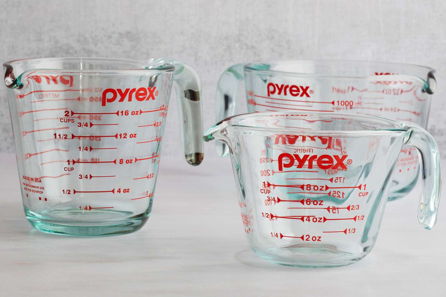 Three glass Pyrex measuring cups on a marble countertop.