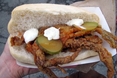 A deep fried soft-shell crab sandwich with pickle slices, mayo, and hot sauce on a split bun.