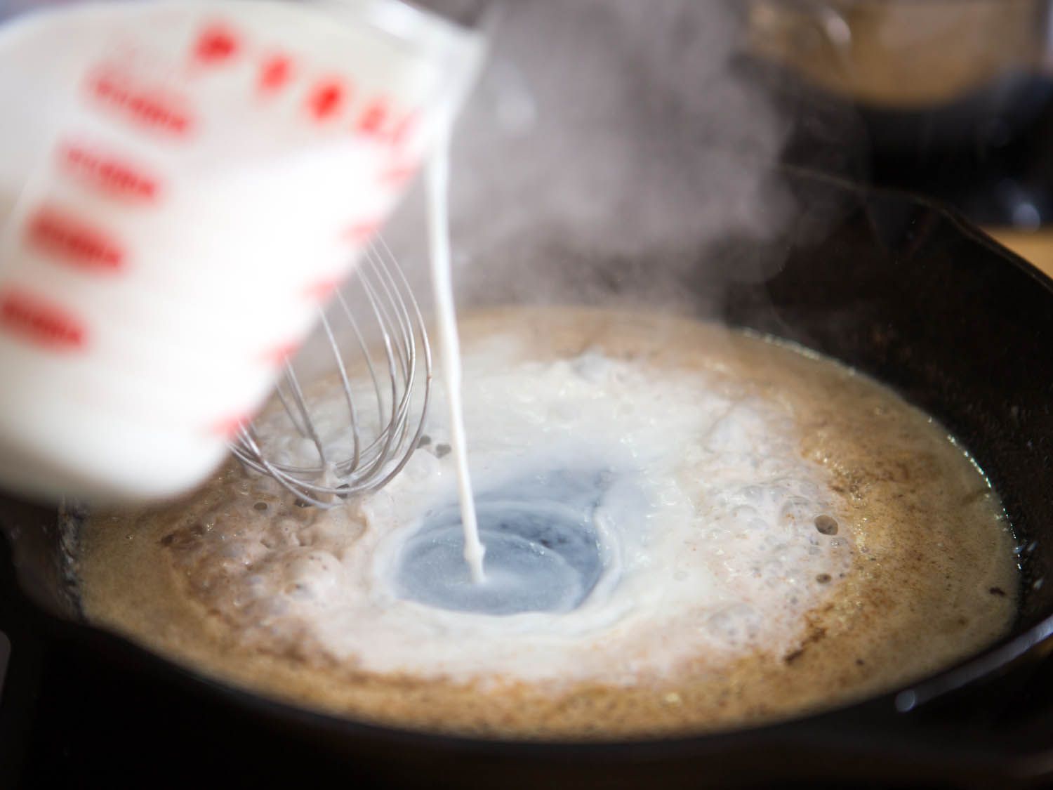 Pouring milk into a pan of roux to make gravy for Maryland fried chicken.