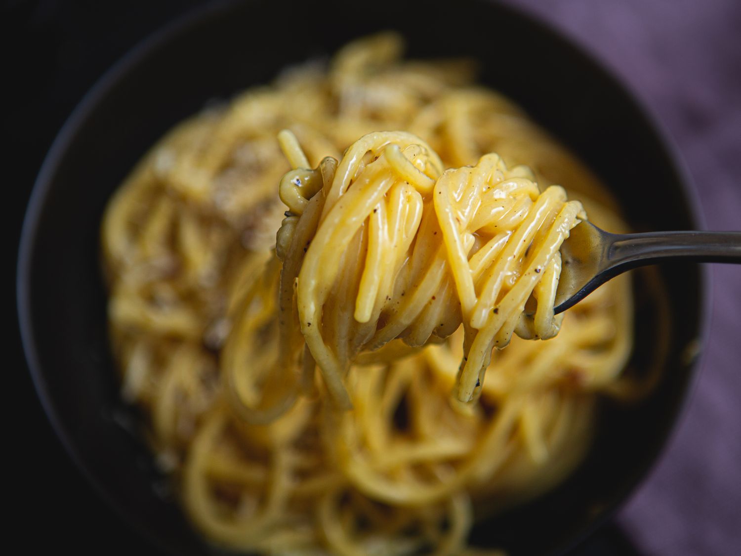 Spaghetti carbonara getting twirled on a spoon.