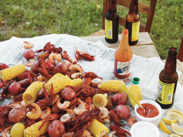 A Low Country boil, served on a picnic table covered in newspaper with cocktail sauce, lemon wedges, hot sauce, and beer.