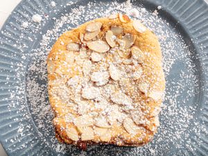 Close up of slice of bostock on a blue plate doused in powdered sugar