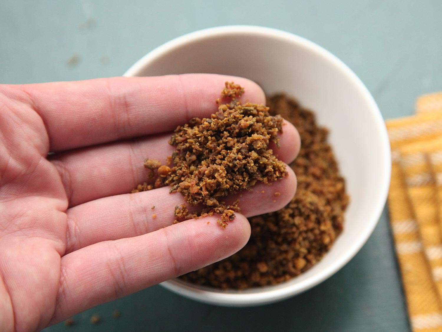 Closeup of hand holding some dried olive and miso shake 
