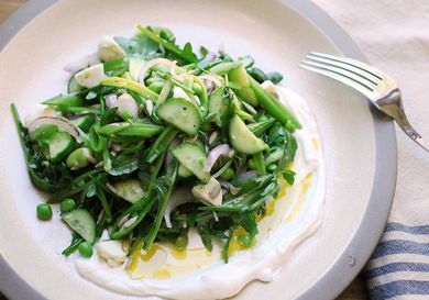 Overhead view of Spring Vegetable and Arugula Salad With Labne and Cucumbers, served on an off-white ceramic plate.