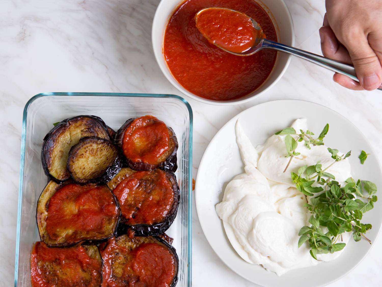 Spooning tomato sauce over layered eggplant for Eggplant Parm.