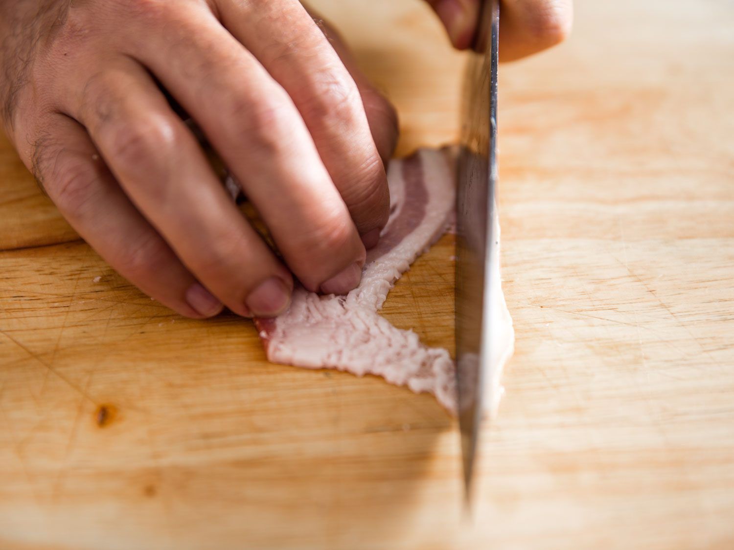 Knife cutting bacon into slices at room temperature.