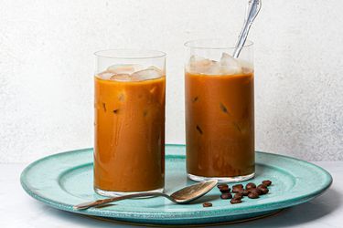Two glasses of Vietnamese iced coffee on a blue plate with coffee beans.