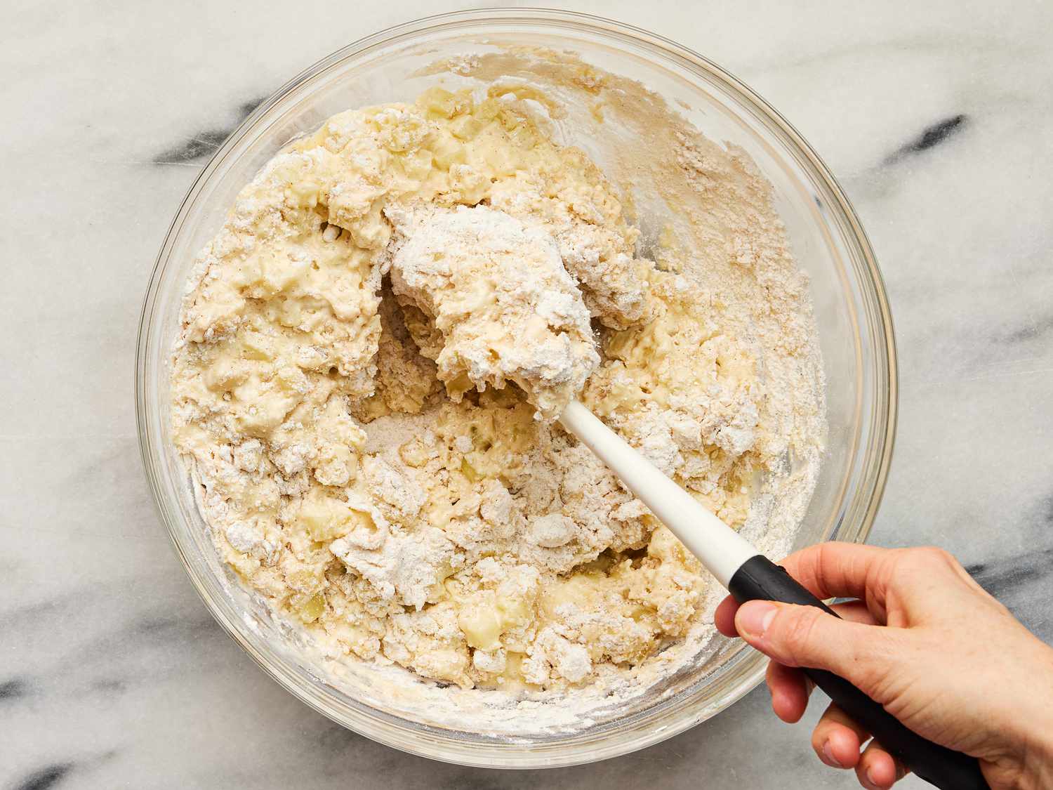 Folding in sour cream mixture and cooked apples to dry mixture with a spatula in a glass bowl 