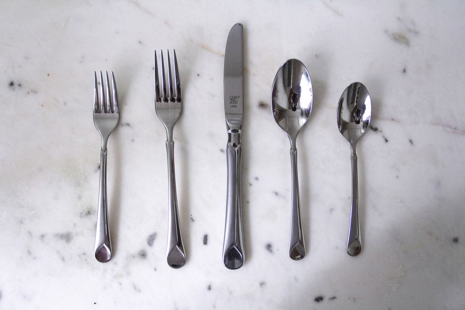 A set of stainless steel cutlery including forks a knife and spoons arranged on a marble surface