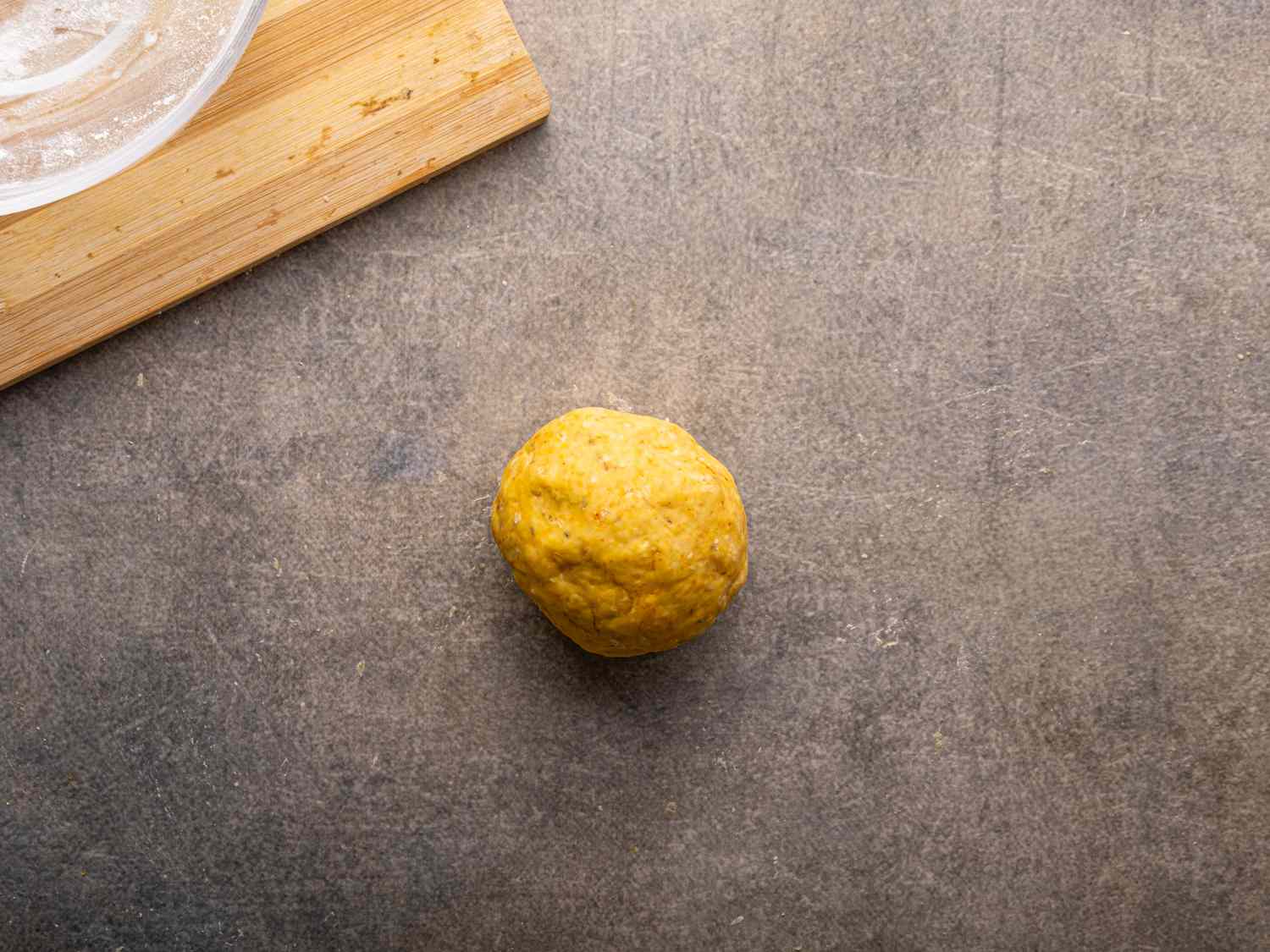 A ball of dough on a flat surface next to a wooden cutting board