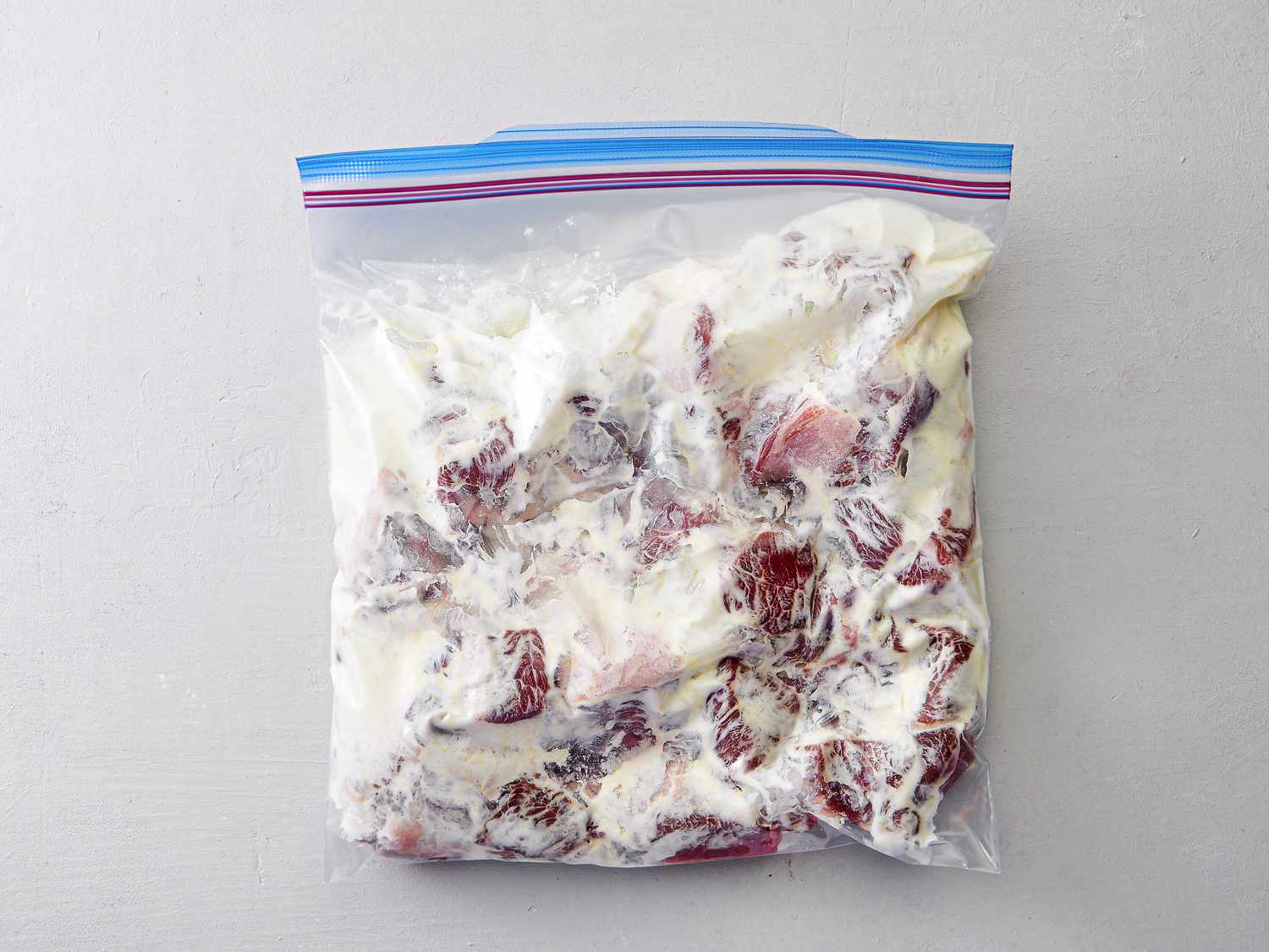 Overhead view of meat in a yogurt marinade in a plastic bag.